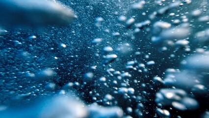 Air bubbles ascending from the ocean floor to the water's surface in slow motion, accompanied by a diver's release of air. Abstract and serene natural background