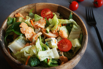 Vegetable salad with chicken and cheese next to a knife and fork on a gray background