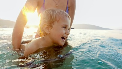 Lasting memories on a family beach vacation with a joyful toddler boy, who can't stop laughing while receiving swimming lessons from his mother during summertime