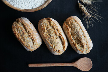 Fresh breads next to spoon and flour on black background