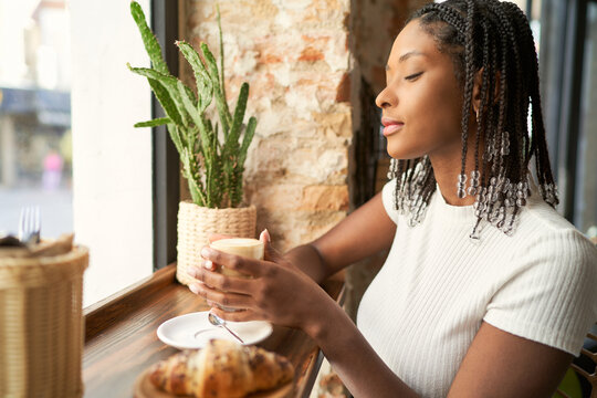 Young pensive black woman student enjoying coffee taste in canteen
