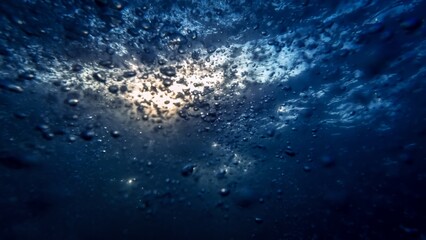 Air bubbles ascend from the seabed to the water's surface, complemented by a diver's exhalation....