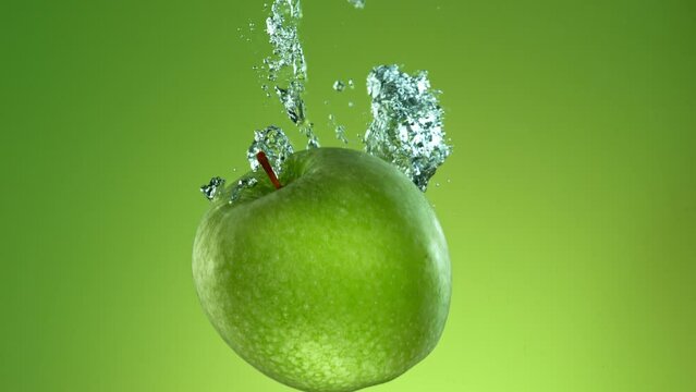 Super slow motion of falling fresh apple into water on green gradient background. Filmed on high speed cinema camera, 1000 fps.
