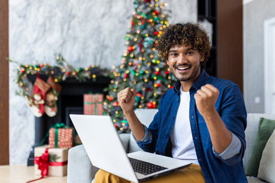 Portrait of a successful winner at home, the man is smiling and looking at the camera, holding hands up in a gesture of triumph and good results of achievement, Christmas and New Year holidays.