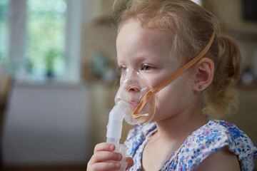 Sick little girl making inhalation with nebulizer to reduce coughing at home, child taking...