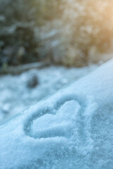 Hand drawn of a heart shape on natural pure bright white soft snow surface in cold weather. A romantic idea for Valentine's day. Winter forest in background.