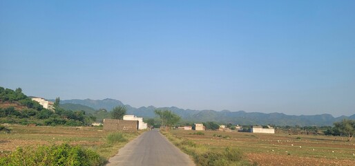 Winding road running through a barren landscape, with a few homes and hills in the distance
