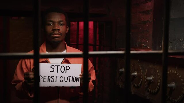 Black man with cardboard with phrase Stop Persecution behind iron bars of jail