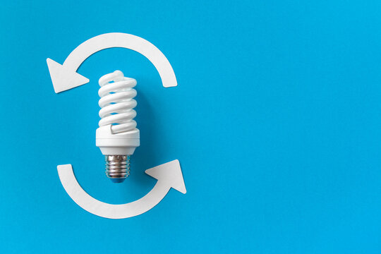 Energy saving light bulb and recycle arrows. Economical consumption of electricity. Blue background copy space. The concept of nature conservation and renewable energy sources
