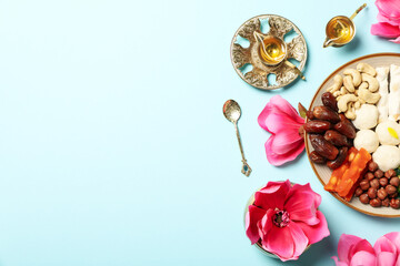 Plate with sweets, copper utensils and flowers on blue background, space for text