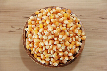 Small round yellow dry corn grains in a plate on a brown background