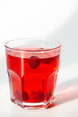 Red cocktail with raspberries in a glass on white, close-up.