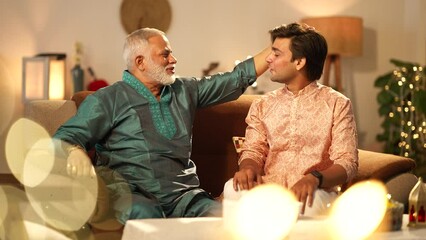 Indian son touching her father's feet on diwali on the sofa and talk to her.they both good looking in traditional dress.decorated background.diwali festival celebration.
