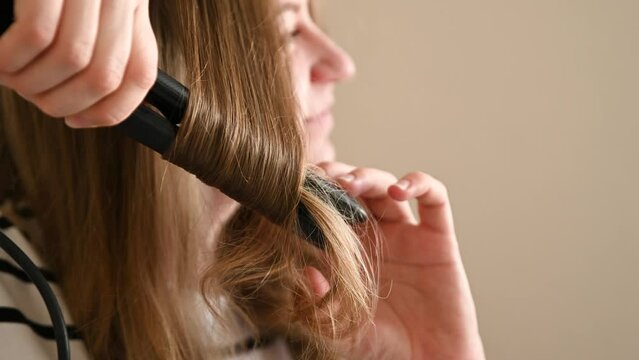 Close-up of a young sexy model woman preparing for a party and photo shoot doing a bun and styling her hair with a hot curling iron