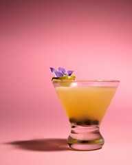 Passionfruit cocktail in a clear glass, garnished with a purple flower, against a pink background