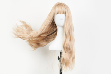Naklejka premium Natural looking blonde wig on white mannequin head. Long hair on the plastic wig holder isolated on white background, front view.