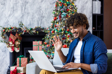 Man sitting home in e living room on sofa for Christmas. Hispanic uses laptop for online video...