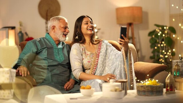 A Indian father and his daughter happily waving and chatting on a video call during Diwali, colourful decorations.a Hindu festival,wearing traditional dress.sitting on the sofa.
