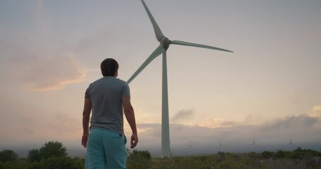 Back view of young man standing against the windmills. Development electric industry business renewable energy of nature