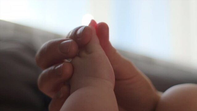 Selective focus of unrecognizable caring young mom massaging arm, fingers and chest of five month baby boy lying on sofa. Close up of little child relaxed, enjoying therapeutic massage. Slow motion