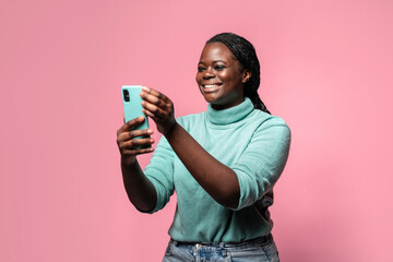 Cheerful african woman using phone against pink background