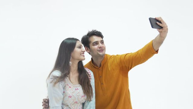 A happy couple uses a smartphone to take a selfie. Attractive couple taking a picture together on a cellphone during diwali festivel.Happy Indian couple clicking good selfies