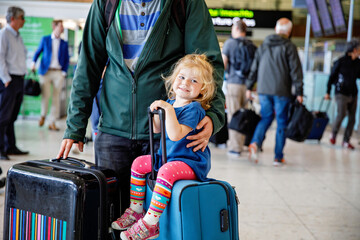 Naklejka premium Cute little toddler girl and father at the airport. Happy family traveling by plane, making vacations. Young dad and baby daughter with suitcases waiting for flight. Family going on journey. Ireland