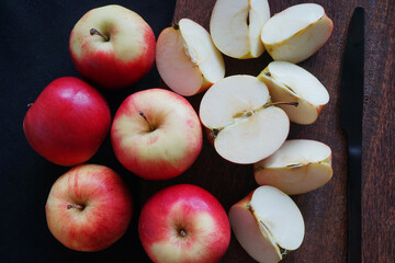 Many apples lie next to a knife on a wooden board