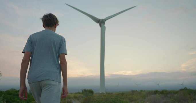 Back view of teenager walking to the windmills. Concept of future humanity. Development electric industry business renewable energy of nature