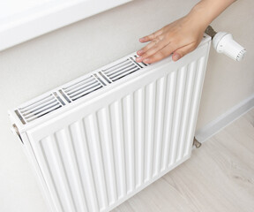 The girl holds her hand near the radiator in the room. The concept of comfortable temperature in the winter in the apartment. Gas heating, sanctions on energy resources. Copy space for text