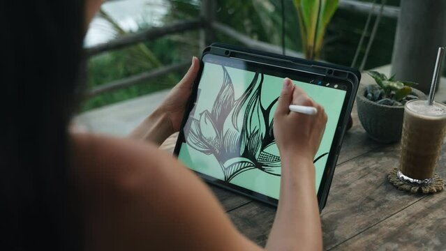 Female illustrator hands draw on tablet at cafe with ocean view, palm trees. Freelancer working outdoor on the terrace at the seaside. Pretty woman drink cappuccino. Close-up, back view.