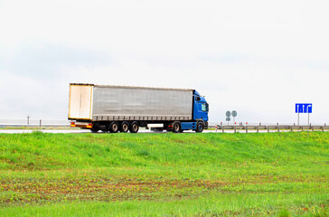 A truck with a semi-trailer transports cargo in summer in cloudy rainy weather on a wet road in the rain. Skidding on the road. Import substitution, export and import of goods. 
