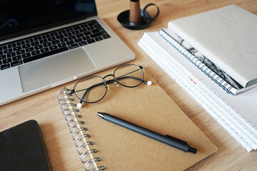 Notebooks with glasses, pen, smartphone, open laptop on wooden table