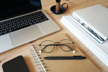 Notebooks with glasses, pen, smartphone, open laptop on wooden table