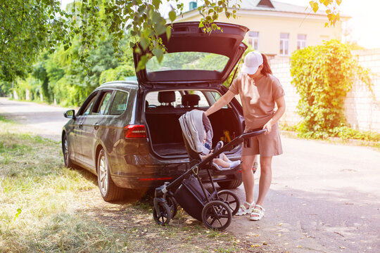 A beautiful girl puts a baby stroller into the open trunk of a car. Traveling in a family car. Copy space for text