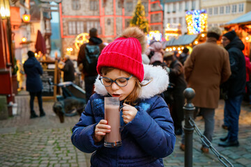 Little cute preschool girl drinking hot children punch or chocolate on German Christmas market. Happy child on traditional family market in Germany, Laughing kid in colorful winter clothes