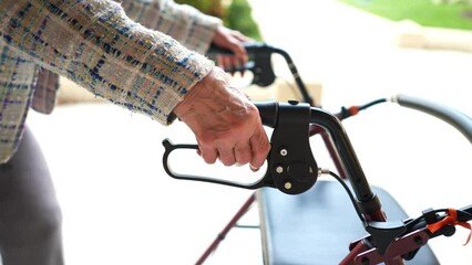 Closeup of elderly senior old caucasian woman hand as she grips handle on walker while walking outside. - Powered by Adobe