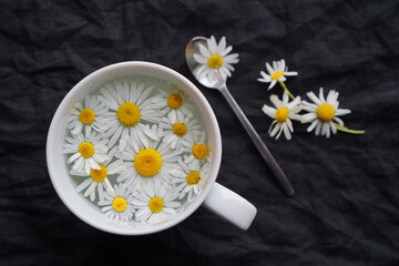 Cup with tea and daisy flowers on a dark background
