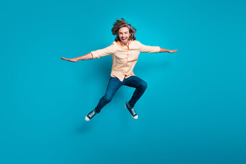 Fototapeta na wymiar Full length photo of carefree guy with long haircut wear stylish shirt flying hold hands like wings isolated on blue color background
