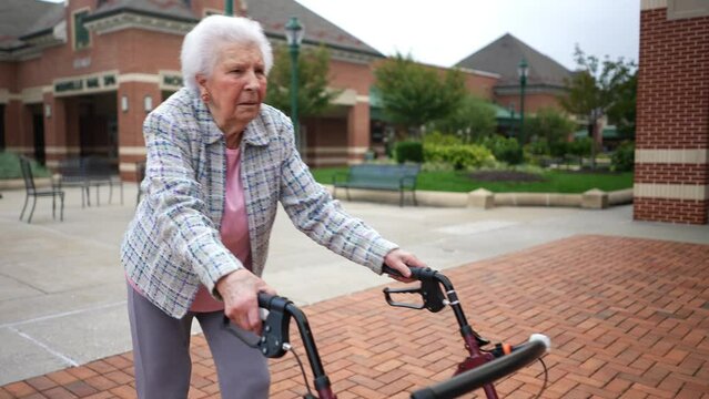 Front view of elderly senior old woman using walker for mobility on sidewalk at shopping center. Concept of independence and aging gracefully.