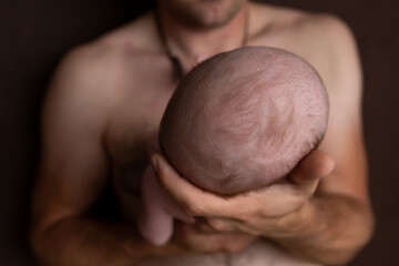 Naklejka premium Father holding head of her newborn baby in hands. Loving father hand holding cute sleeping newborn baby child. Beautiful conceptual image of parenthood