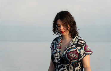 View of a young woman against the background of a calm lake at sunset