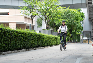 Businesswoman with helmet riding bicycle on road go to work at office. Happy woman commuting on bike in city. Eco friendly vehicle, sustainable lifestyle concept.