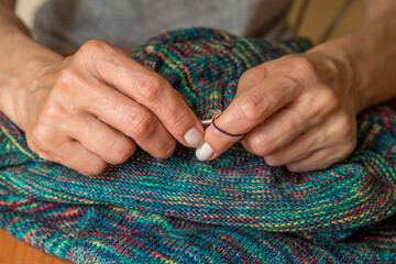 Close up of hands of unrecognizable woman knitting handmade clothes with spokes using  wool yarn....