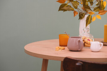 Autumn home decoration. Vase with autumn leaves, two glasses of tea, cookies on green background.