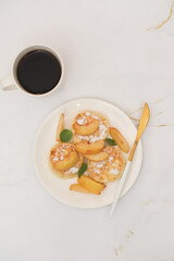 Cottage cheese pancakes with peach and mint leaves, coffee on a white plate on a light background.