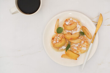 Cottage cheese pancakes with peach and mint leaves on a white plate on a brown background.