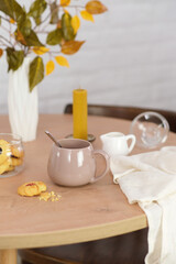 Autumn home decoration. Vase with autumn leaves, glasse of tea, cookies on wooden table and white background.