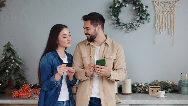 Portrait of Caucasian couple in love shopping online on smartphone and buying with credit card enjoying christmas sales. Female speak cvv code to husband for purchase gift on internet Holidays concept