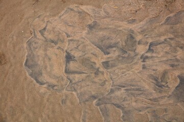 Abstract patterns on sand surface on the beach shore caused by waves washing over the sand.